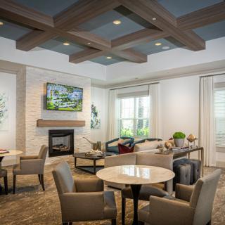 A modern living room featuring a cozy seating area with tables, chairs, a fireplace, and a television mounted above.