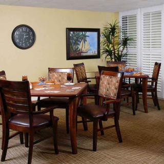 A cozy dining room with wooden tables and chairs, featuring a wall clock and a painting for decoration.