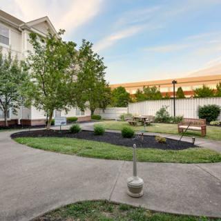 A well-maintained garden with a walkway, trees, and benches in a residential area.