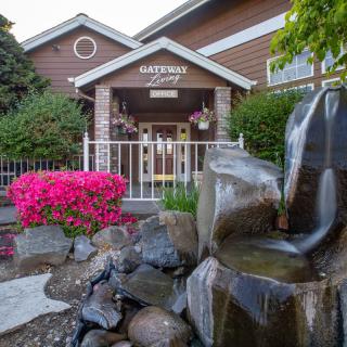 A scenic view of a building entrance featuring a water fountain and vibrant garden flowers.