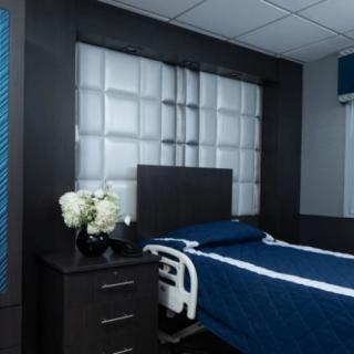 A modern hospital room with a single bed and blue bedding, featuring a sleek design and decorative flowers on a nightstand.