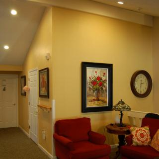 A cozy living room corner with red chairs, a table lamp, wall clock, and framed artwork.