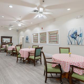 A modern dining area with neatly arranged tables and chairs, featuring ceiling fans and decorative artwork on the walls.