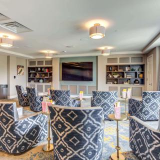 A modern lounge with patterned chairs, built-in bookshelves, and a large television.