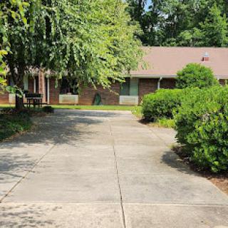A view of a residential house with a paved driveway surrounded by greenery.