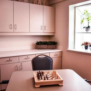 A cozy room with a chessboard on the table, surrounded by cabinets and natural light from the window.