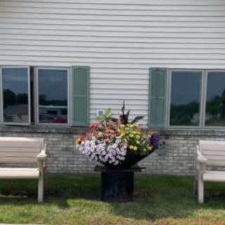 Outdoor flower arrangement between two benches in front of a building.
