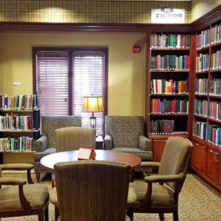 A cozy library reading area with bookshelves, chairs, and a table under warm lighting.