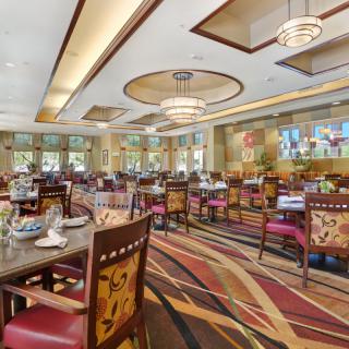 A spacious and elegantly designed restaurant dining area featuring stylish chandeliers, patterned carpets, and neatly arranged tables and chairs.