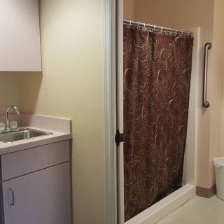 A bathroom with a sink, cabinet, and shower area with a curtain and handrail.