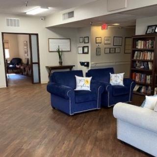 A cozy living room featuring blue and white couches, a bookshelf, and warm wooden flooring.