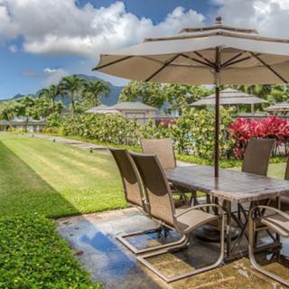 A scenic patio setup with outdoor furniture and an umbrella, overlooking a lush garden and lawn.