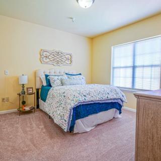 A cozy bedroom with a neatly made bed, side table, and large window.