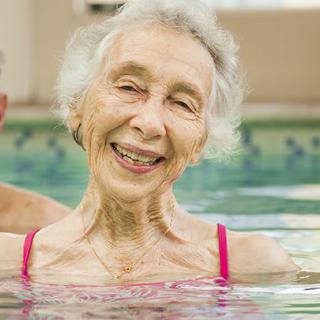 An elderly woman smiling while enjoying her time in a swimming pool.