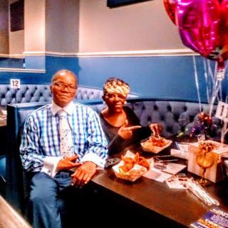 A couple enjoying a meal at a restaurant, celebrating with balloons and gifts on the table.