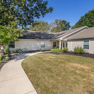 A single-story house with a landscaped yard and concrete pathway leading to the entrance under a clear blue sky.