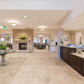 A spacious and well-decorated lobby featuring a central fireplace, tiled flooring, and a reception desk.