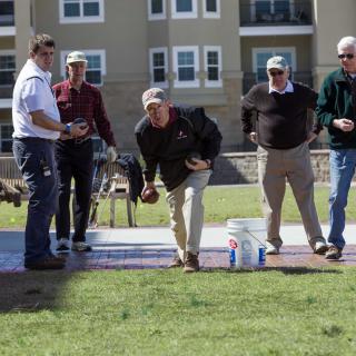A group of people playing bocce ball outside on a sunny day.