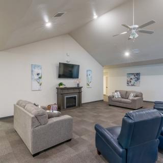 A spacious living room featuring comfortable sofas and armchairs, a television mounted above a fireplace, and a ceiling fan overhead.