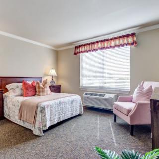 A cozy bedroom with a neatly made bed, an armchair, and a window allowing natural light to brighten the room.