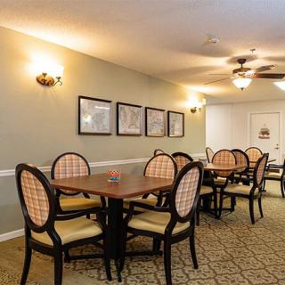 A well-lit dining room with multiple tables and chairs, decorated with framed pictures on the wall.