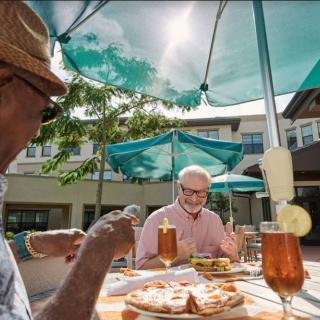 Elderly friends enjoying a sunny meal outdoors under umbrellas.