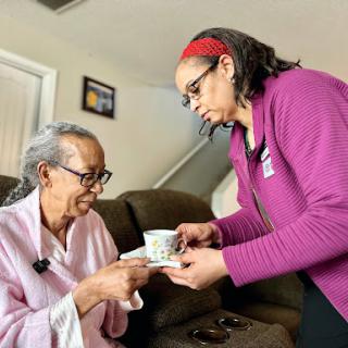 A caregiver serves tea to an elderly woman, highlighting the bond of care and companionship in a cozy home environment.
