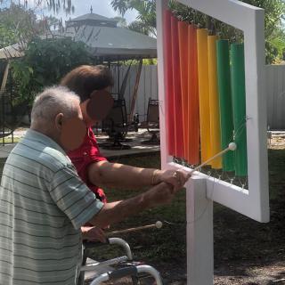 Two people playing a colorful outdoor xylophone in a garden setting.