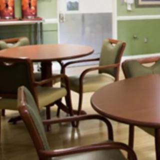 A dining area with round tables and cushioned chairs, set against green walls.