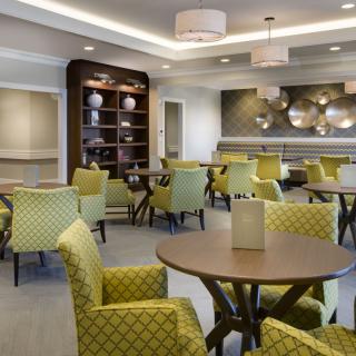 A modern dining area with stylish tables and green patterned chairs, complemented by contemporary lighting and decorative shelving.