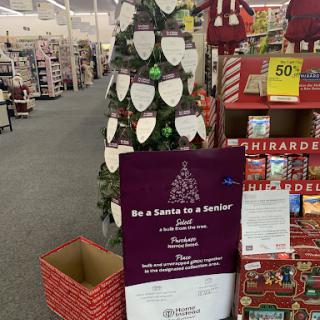 A festive store display featuring a Christmas tree and information about a gift-giving initiative.