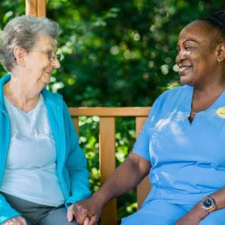 A nurse and an elderly woman share a moment of companionship outdoors.
