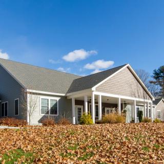 A suburban house with autumn leaves covering the front yard under a blue sky.