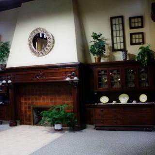 A cozy living room interior with a wooden paneled fireplace, decorative plates, and lush plants.