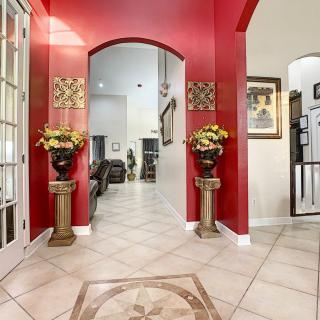 A modern foyer featuring a red accent wall, decorative vases, and artwork, leading into a living space with tiled flooring.