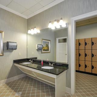 A well-lit bathroom with dual sinks and mirrors, adjacent to a locker area.