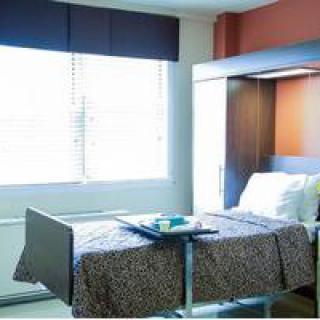 A hospital room with a single bed and a window allowing natural light.