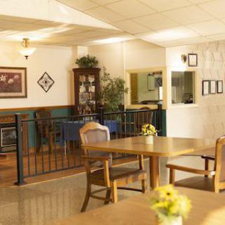 A cozy dining room featuring wooden tables and chairs, decorated with flowers and artwork.
