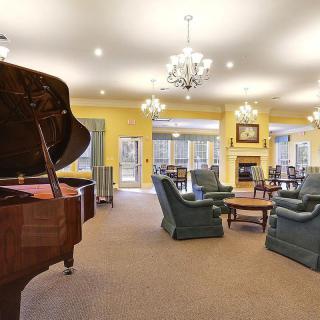 A spacious and luxurious living room featuring a grand piano, elegant chandeliers, and a comfortable seating area around a fireplace.