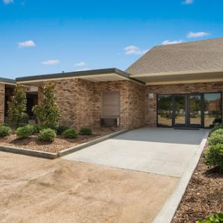 A welcoming entrance to a well-maintained commercial building with lush landscaping and a clear blue sky.