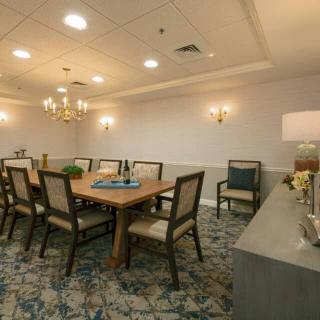 A well-lit conference room with a long wooden table surrounded by chairs and elegant chandeliers.