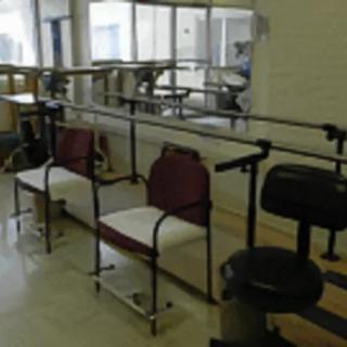A rehabilitation room with parallel bars and chairs used for physical therapy exercises.