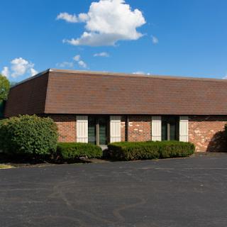 A charming brick office building surrounded by well-maintained shrubs and a clear blue sky.