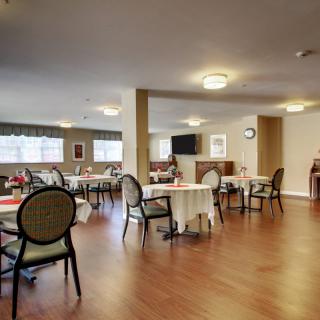 A spacious dining area with multiple tables and chairs, featuring soft lighting and wooden flooring.