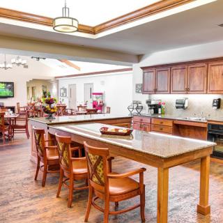 A spacious kitchen and dining area featuring a long wooden table with chairs, wooden cabinets, and bright overhead lighting.