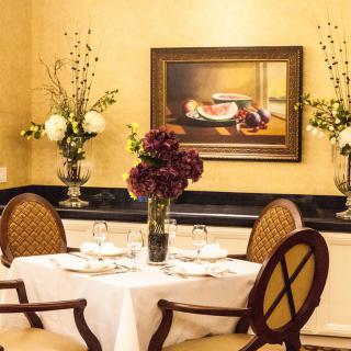An elegantly set dining table with a floral centerpiece and framed painting in the background.