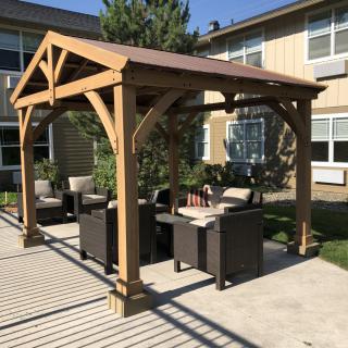 A wooden pergola with comfortable patio furniture set in a sunny backyard.