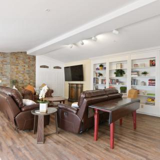 A modern living room featuring comfortable leather sofas, built-in bookshelves, and a large television, all set on elegant wooden flooring.
