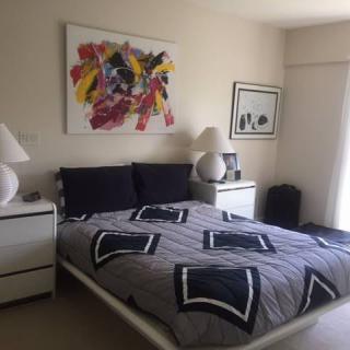 A modern bedroom with abstract art above the bed and stylish lamps on the nightstands.