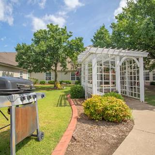 A beautifully landscaped garden with a pergola and grill set in a sunny outdoor setting.